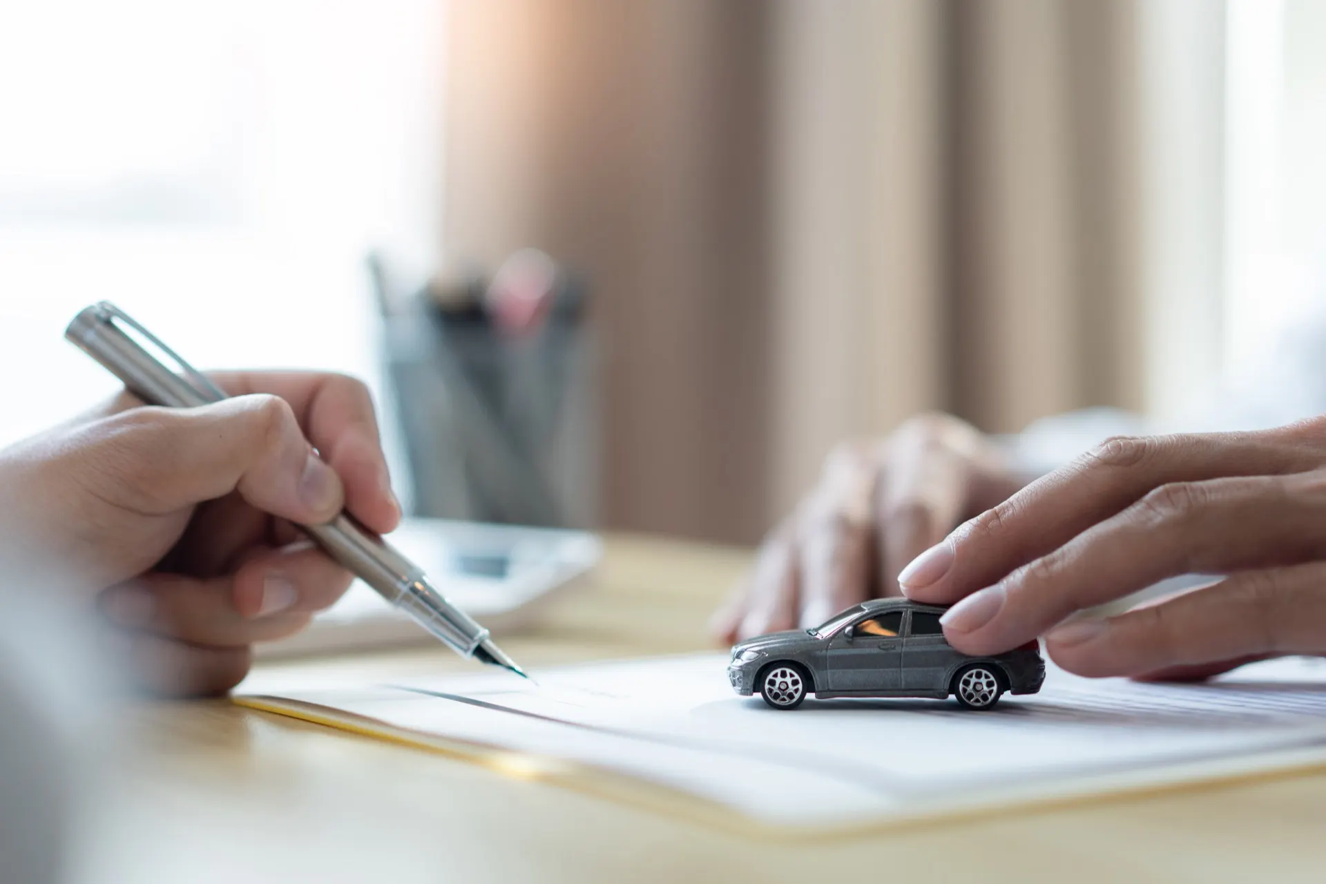 Pessoa assinando documento sobre a mesa, com miniatura de carro ao lado